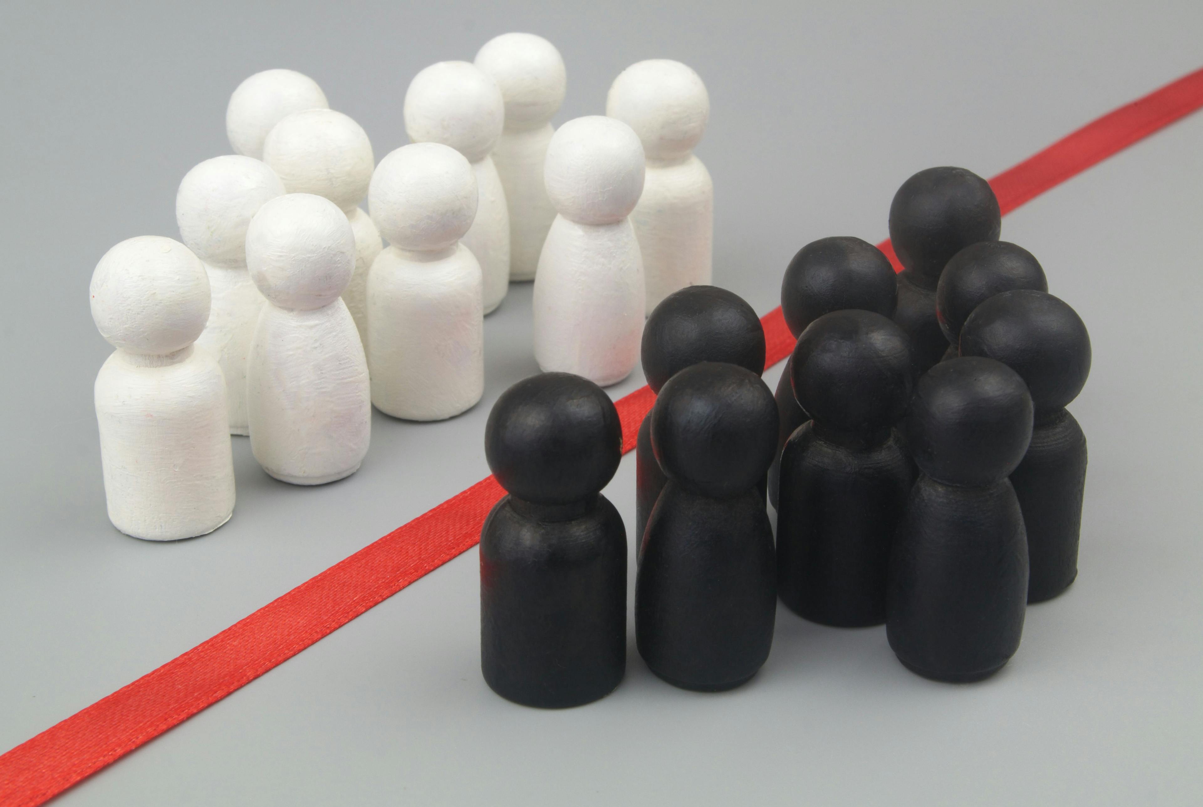 Groups of white and black people figures separated by red line on gray background.